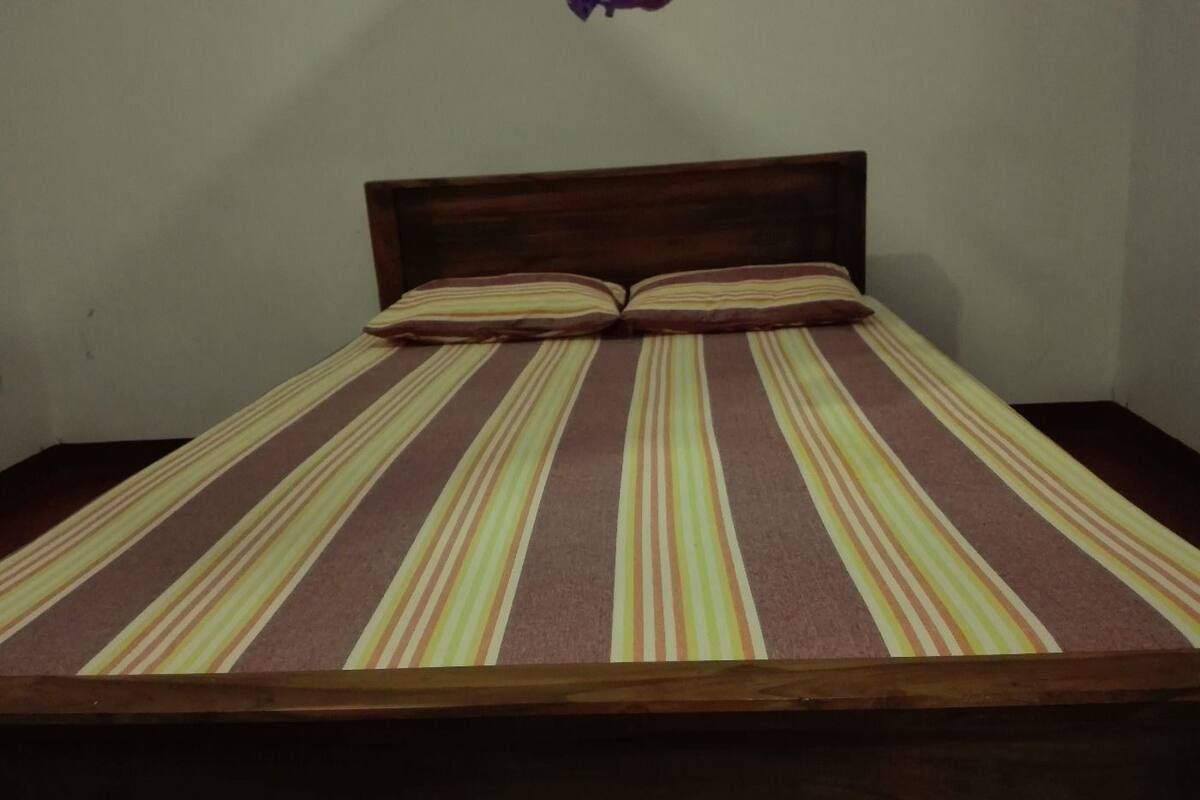 Una cama con una colcha a rayas y dos almohadas, un cabecero de madera y una pared lisa.