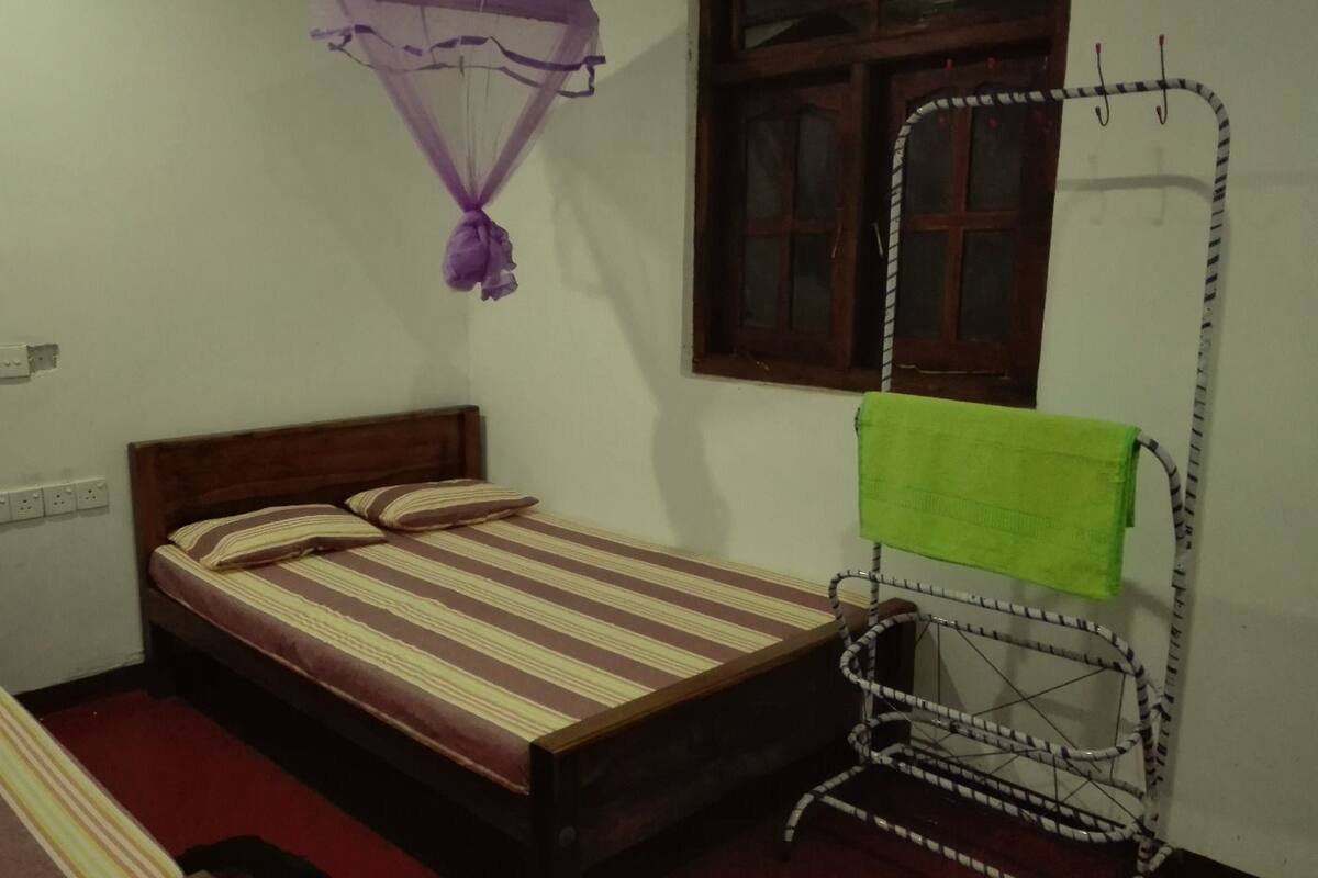 Una cama individual con una colcha a rayas, una toalla verde en un perchero y una mosquitera colgada sobre la cama.