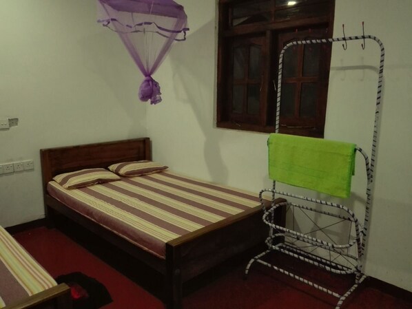 A single bed with a striped bedspread, a green towel on a rack, and a mosquito net hanging above the bed. - Mango shade (Udawalawa)