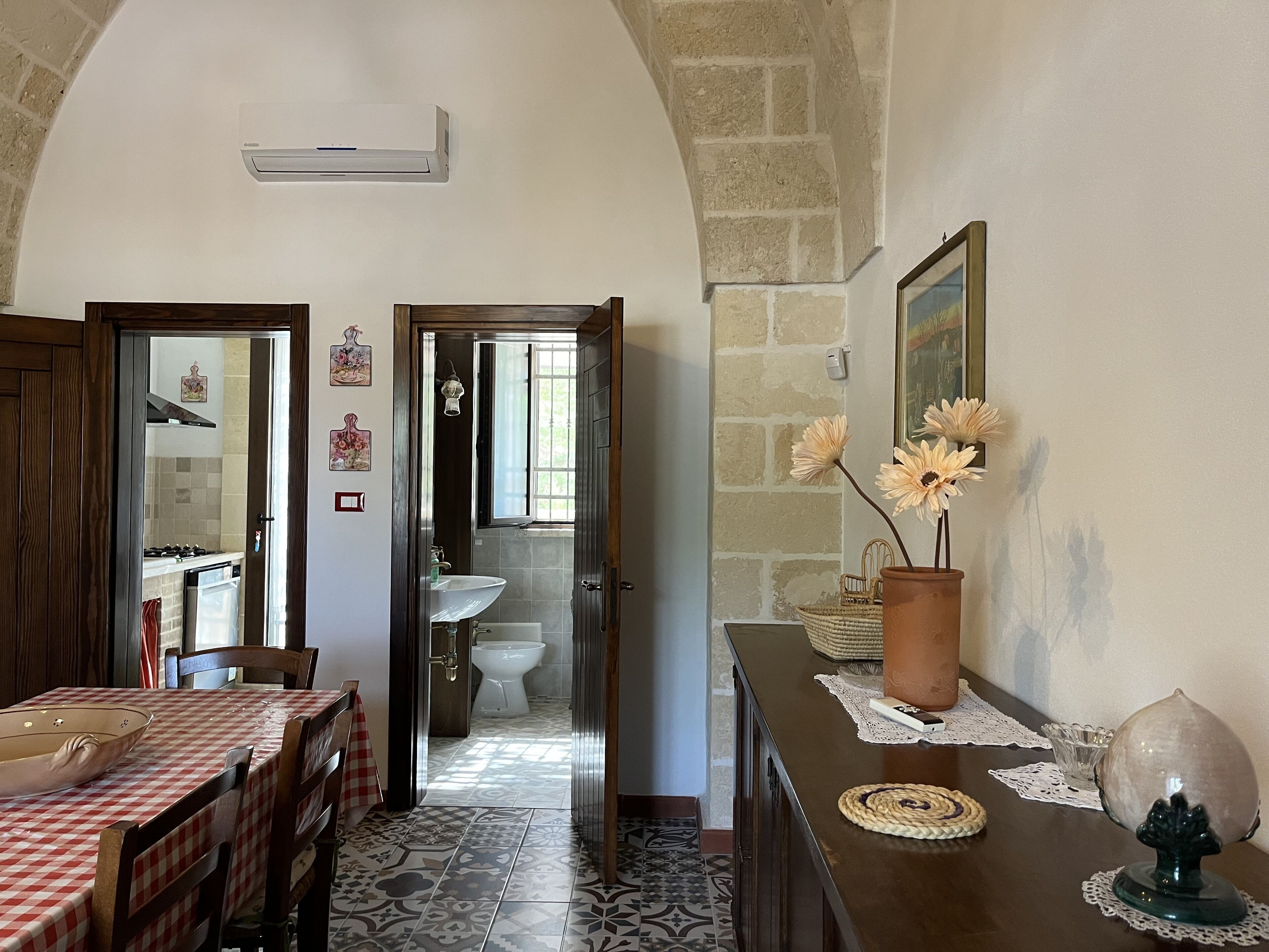 A dining area with a checkered tablecloth, a vase with flowers, and a rustic stone wall.