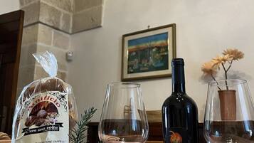 Un tavolo con pane, pomodori, cetrioli e una bottiglia di vino in una stanza con pareti in pietra e un quadro appeso.