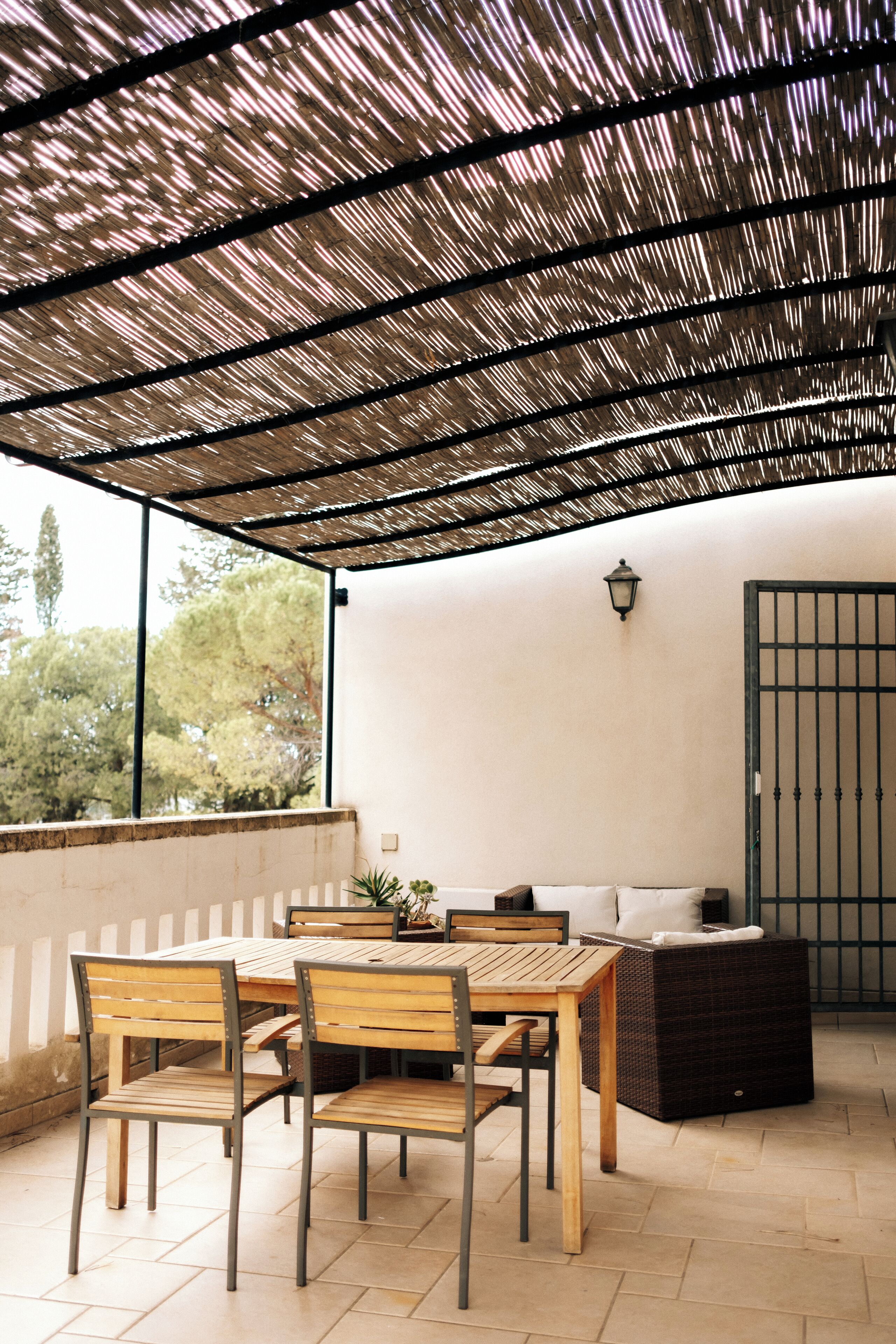 An outdoor patio with a wooden table and chairs, a wicker sofa, and a metal gate.