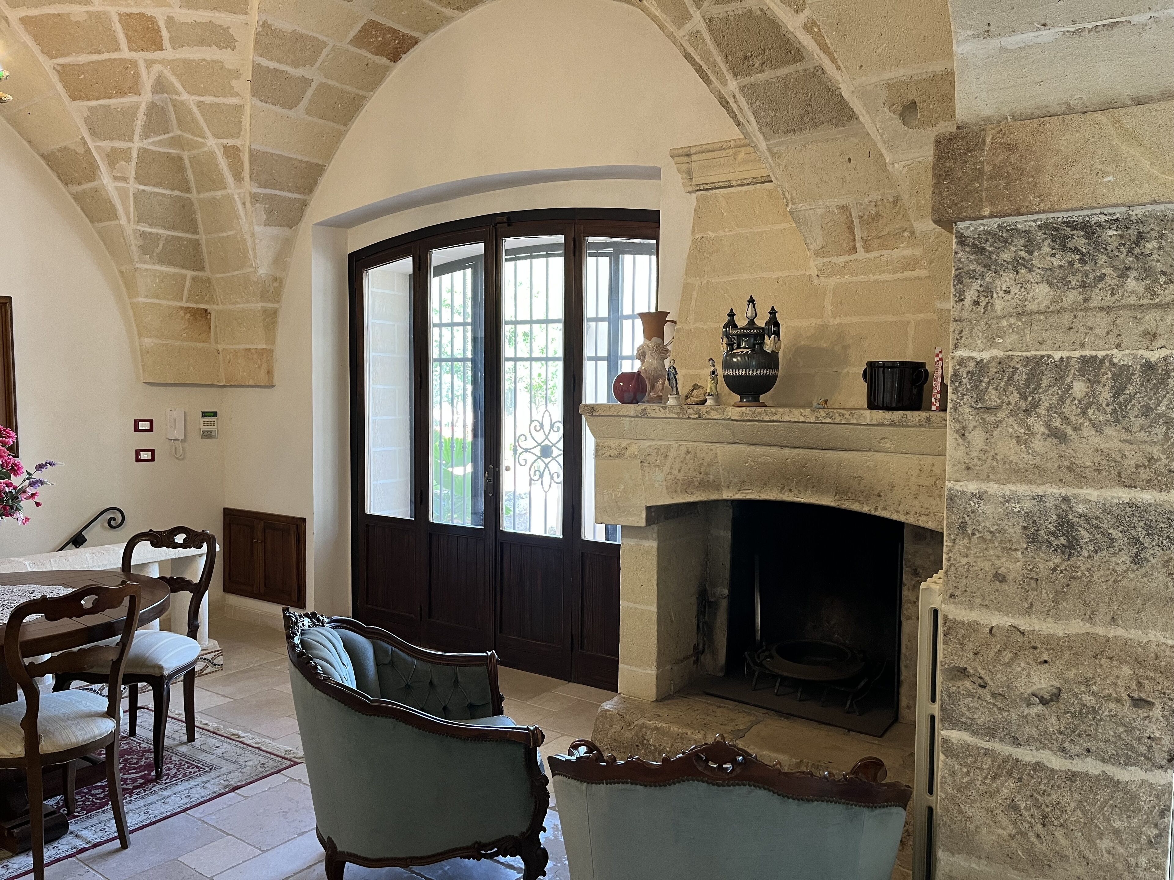 Una habitación con chimenea de piedra, una puerta arqueada con paneles de vidrio y una zona de comedor con mesa y sillas.