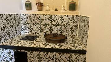 A kitchen with patterned tiles, a pot on the counter, and a shelf with various kitchen items.