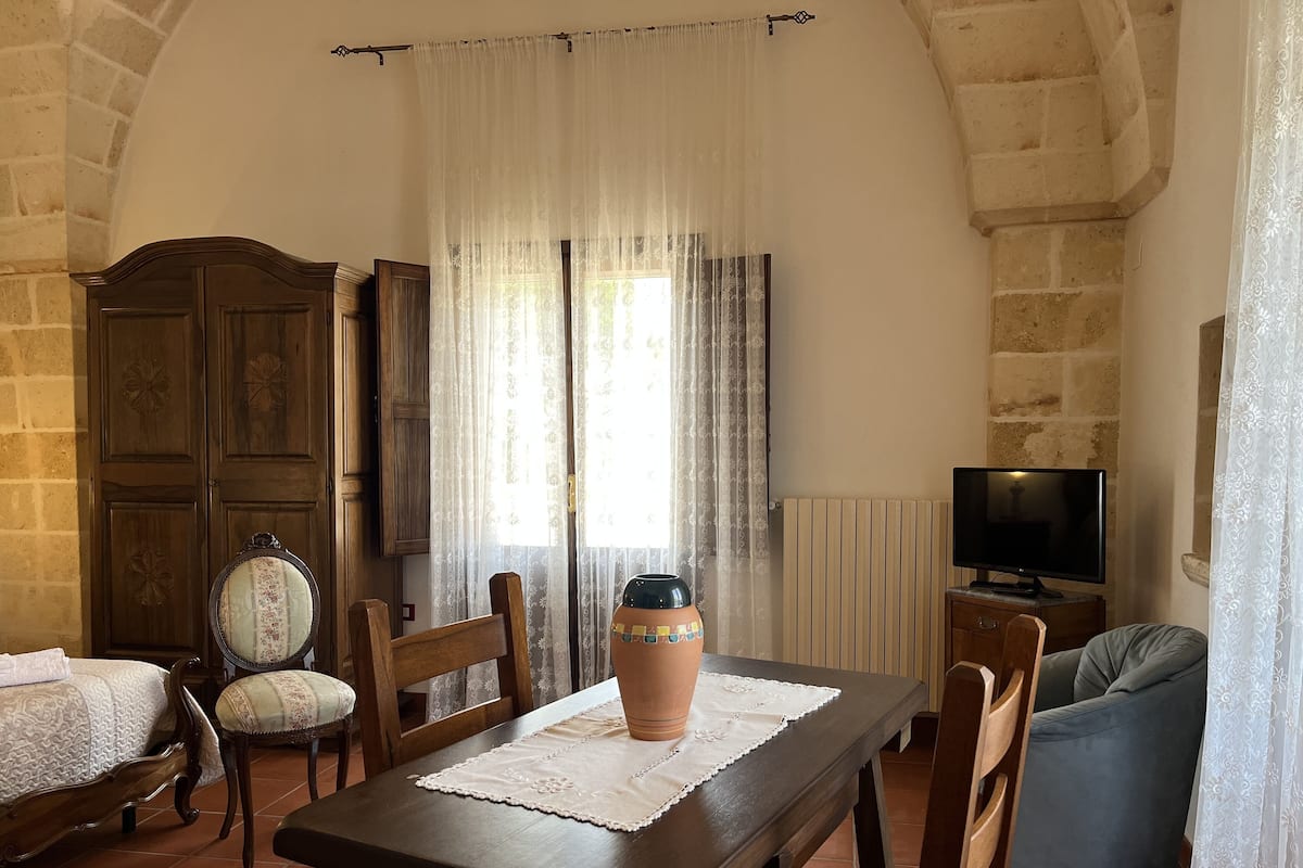 A cozy room with a wooden table, chairs, a TV, and a large window with curtains.