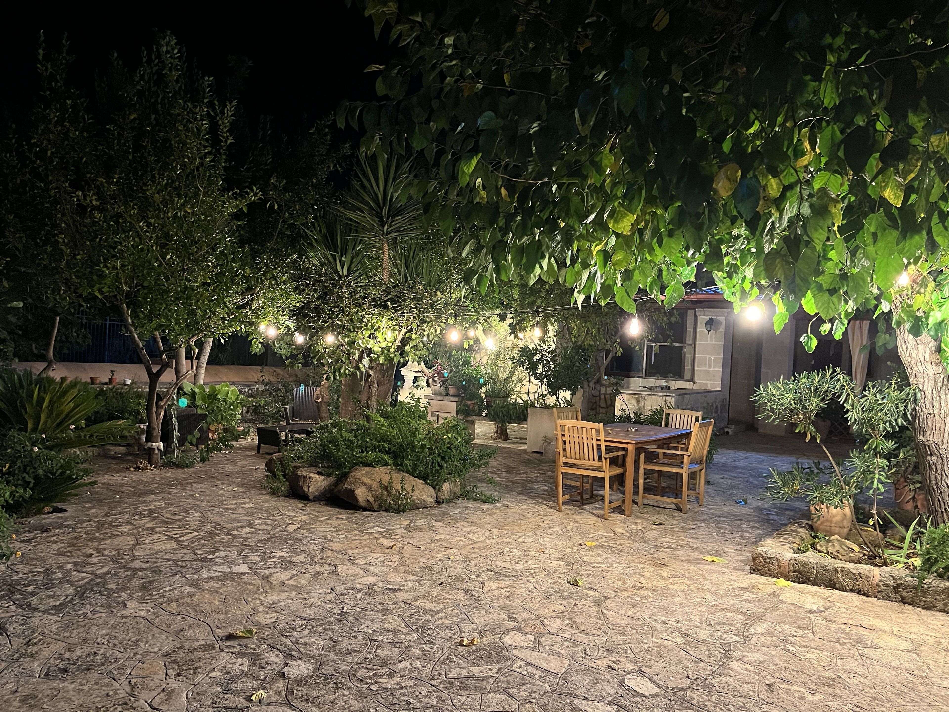 Un espace extérieur aménagé en terrasse, avec un sol en pierre, des meubles en bois et des guirlandes lumineuses.