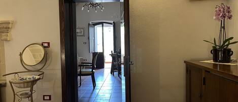 Um corredor com uma porta de madeira que dá para uma sala de jantar, uma pequena mesa com um vaso e uma planta em um balcão.