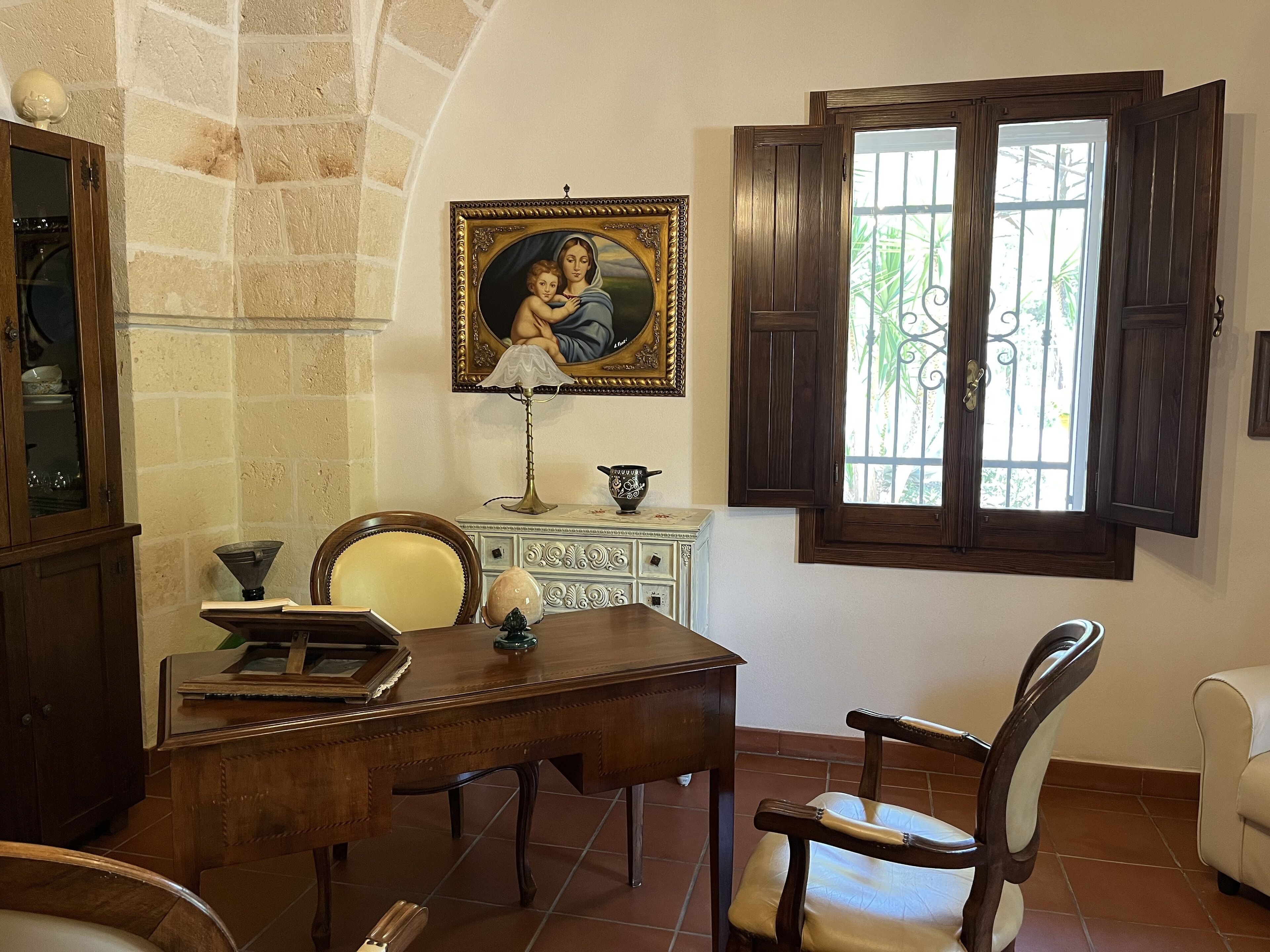 A dining area with a wooden table, chairs, a cabinet, and a window with open shutters.