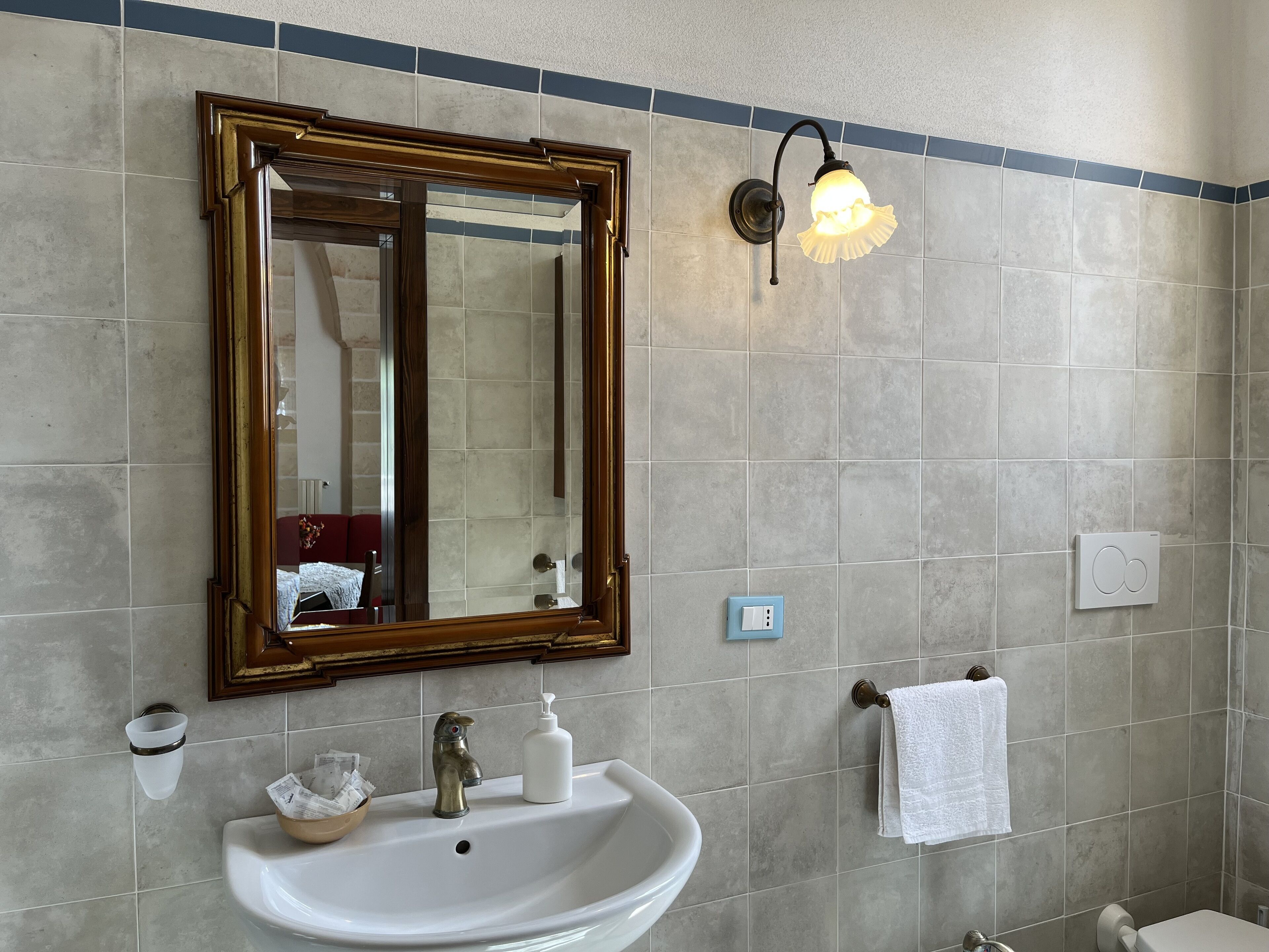 Ein Badezimmer mit großem Spiegel, Waschbecken, Handtuchhalter und einer Wandleuchte.