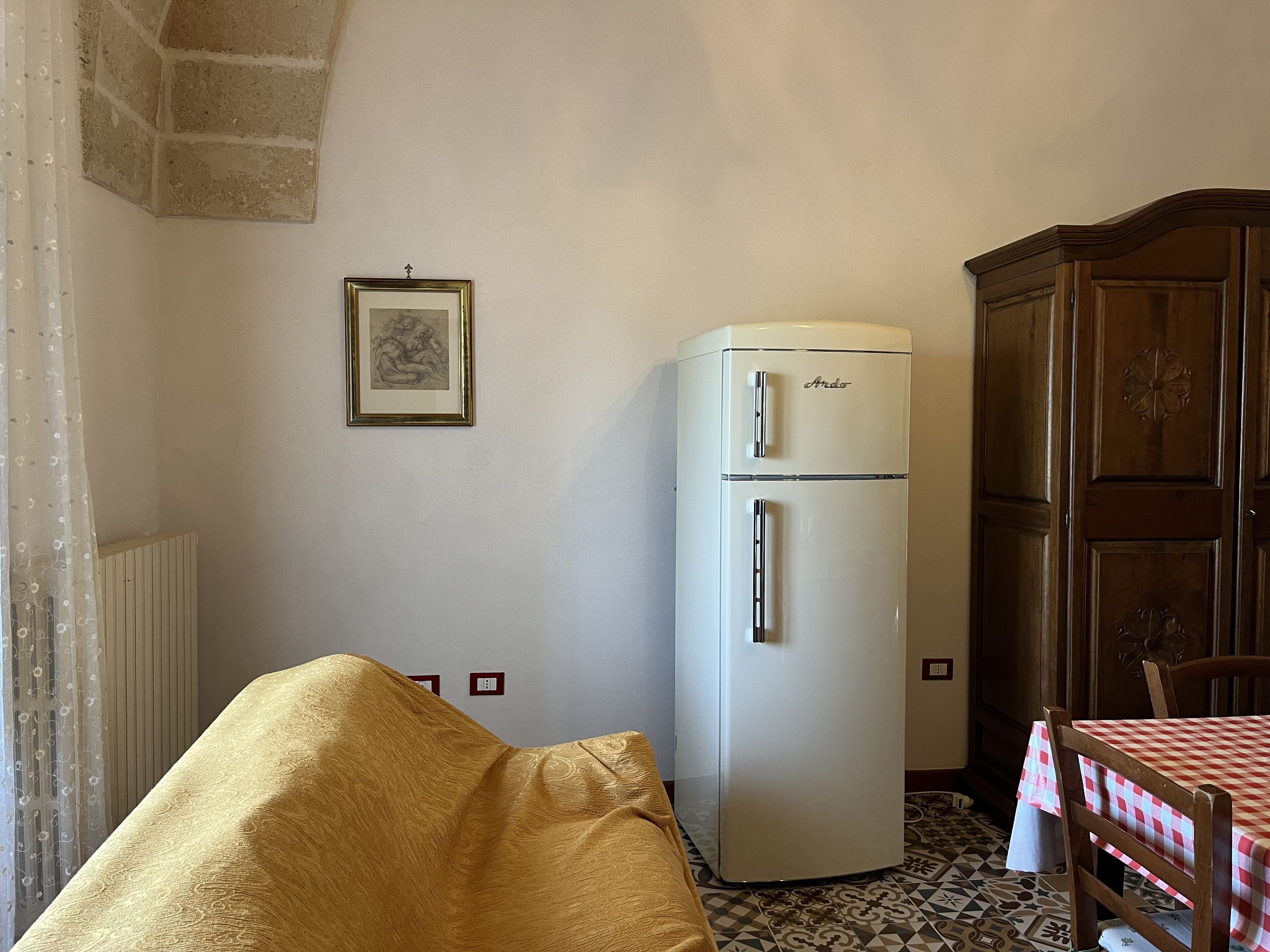 Habitación pequeña con un refrigerador blanco, un armario de madera, un cuadro en la pared y una mesa cubierta con mantel a cuadros.