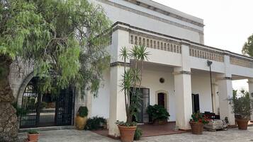 A building with a white facade, large windows, and a covered entrance area with potted plants.