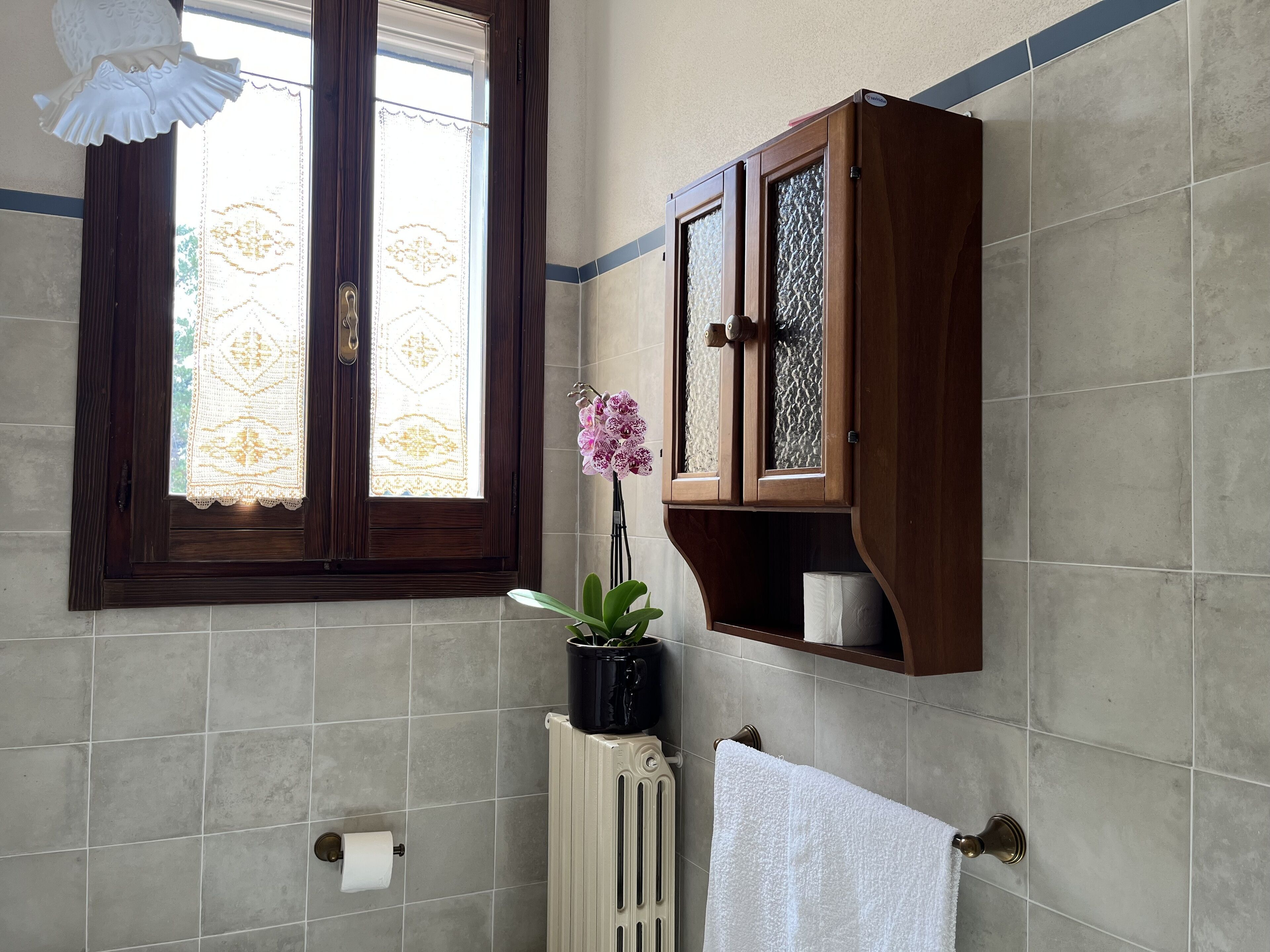 A bathroom with a window, a radiator, a towel rack, and a wooden cabinet.