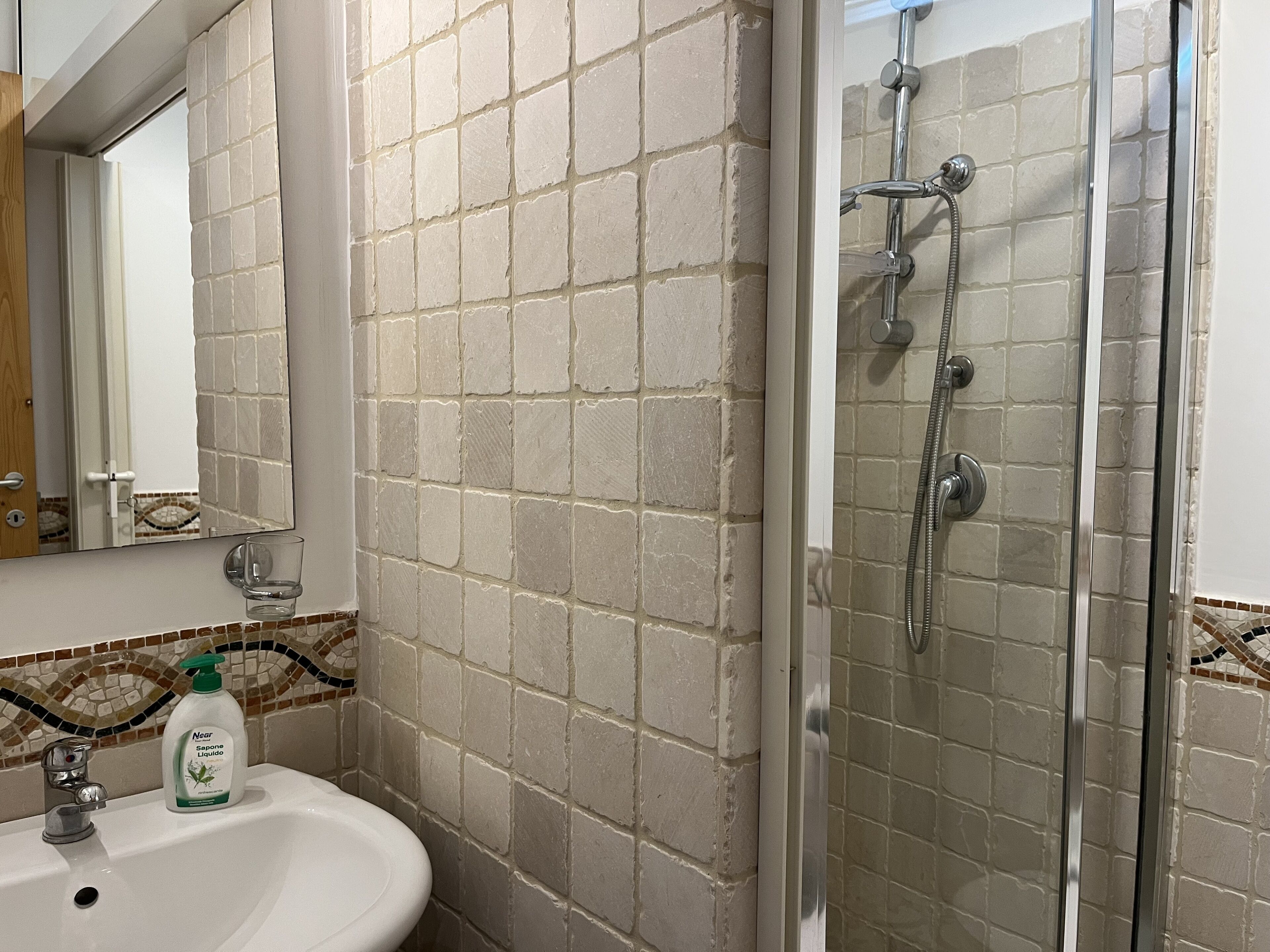 Une salle de bain équipée d’un lavabo, d’un miroir, d’une douche et de murs carrelés.