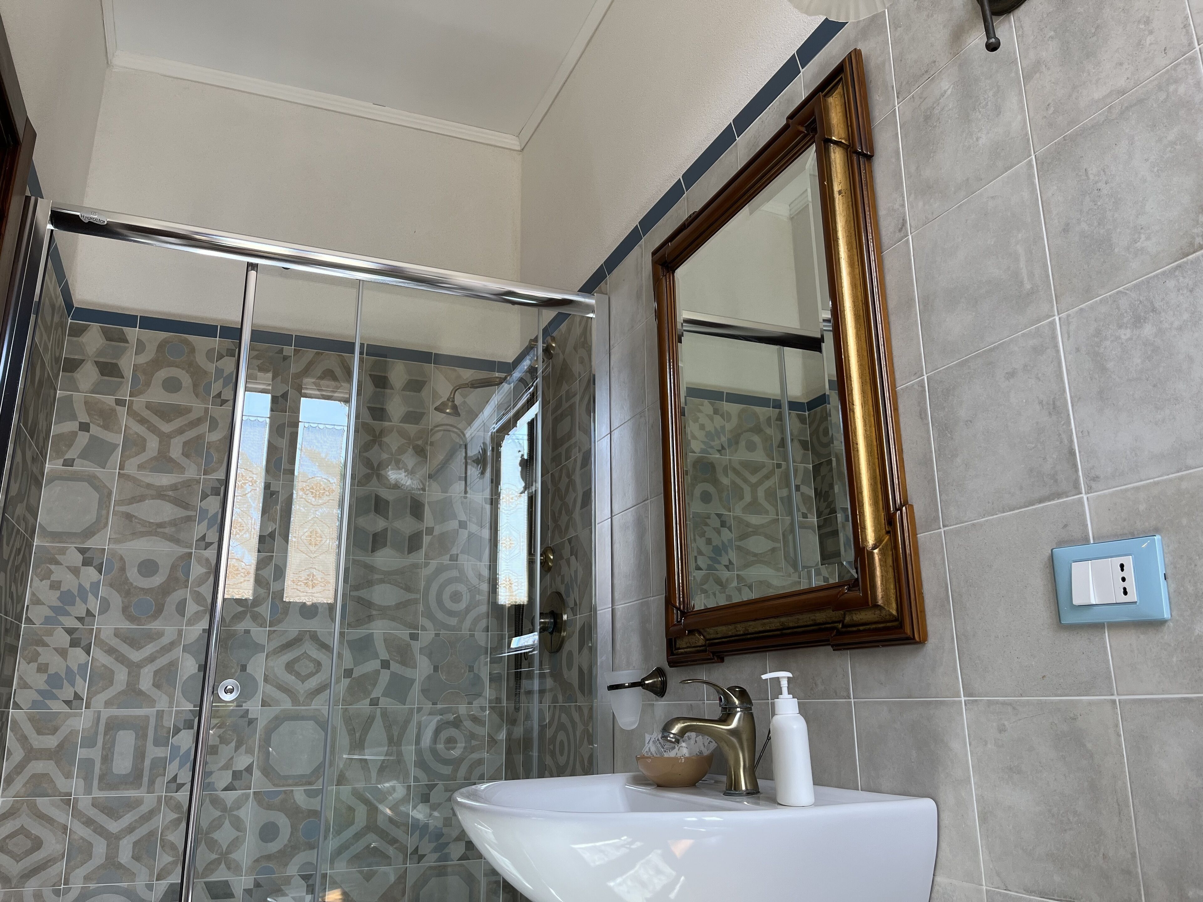 Une salle de bain dotée d’une douche à parois de verre, d’un lavabo blanc, d’un robinet doré et d’un miroir avec un cadre doré.