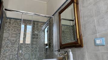 Une salle de bain dotée d’une douche à parois de verre, d’un lavabo blanc, d’un robinet doré et d’un miroir avec un cadre doré.