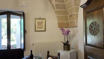 Un coin repas avec une table dressée pour deux personnes, une bouteille de vin et deux verres. Sur la table, on aperçoit une orchidée en pot, un tableau encadré est accroché au mur et un radiateur se trouve en dessous.