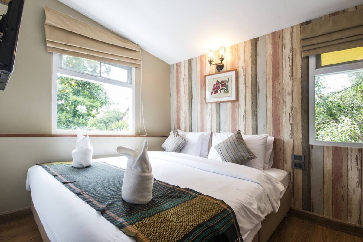 A neatly made bed with a patterned blanket, a framed picture on the wall, and a window with curtains.