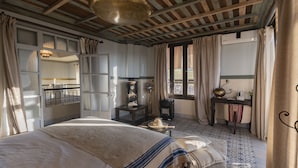 A bedroom with a large bed, a small table, a chair, a window with curtains, and a view of the outside. - Dar Tafantant (Ourika)
