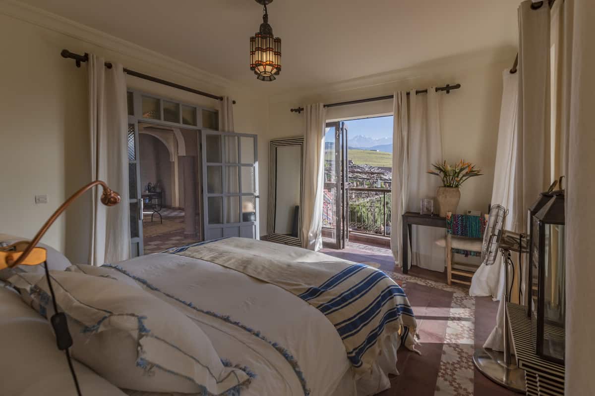 A bedroom with a large bed, a desk, and a view of the outdoors.