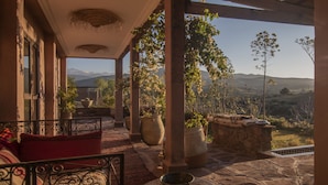 A covered patio with a view of mountains, a stone table with a bowl, and red cushions on a metal chair. - Dar Tafantant (Ourika)