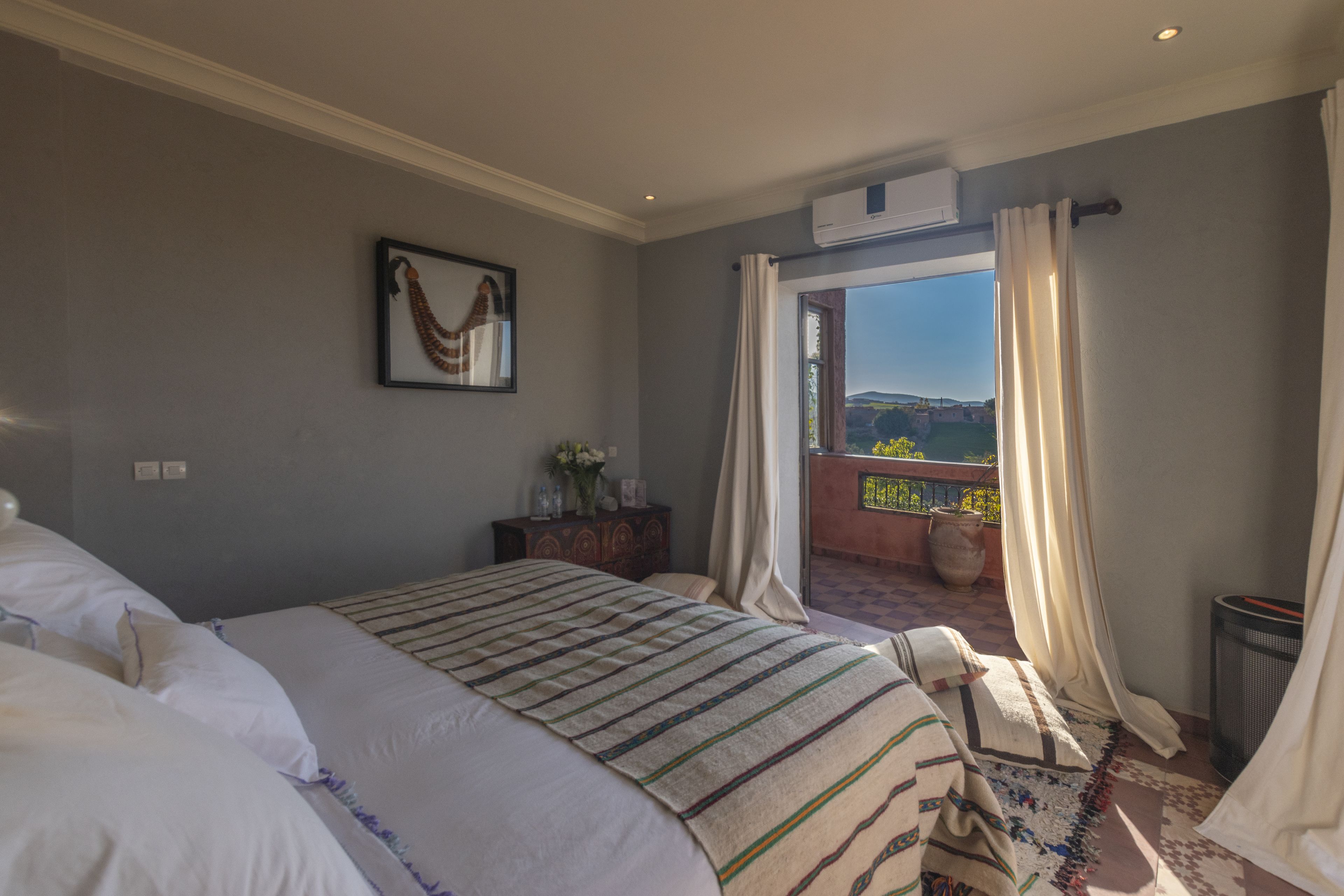 A bedroom with a large bed, a view of the outdoors, and a balcony.
