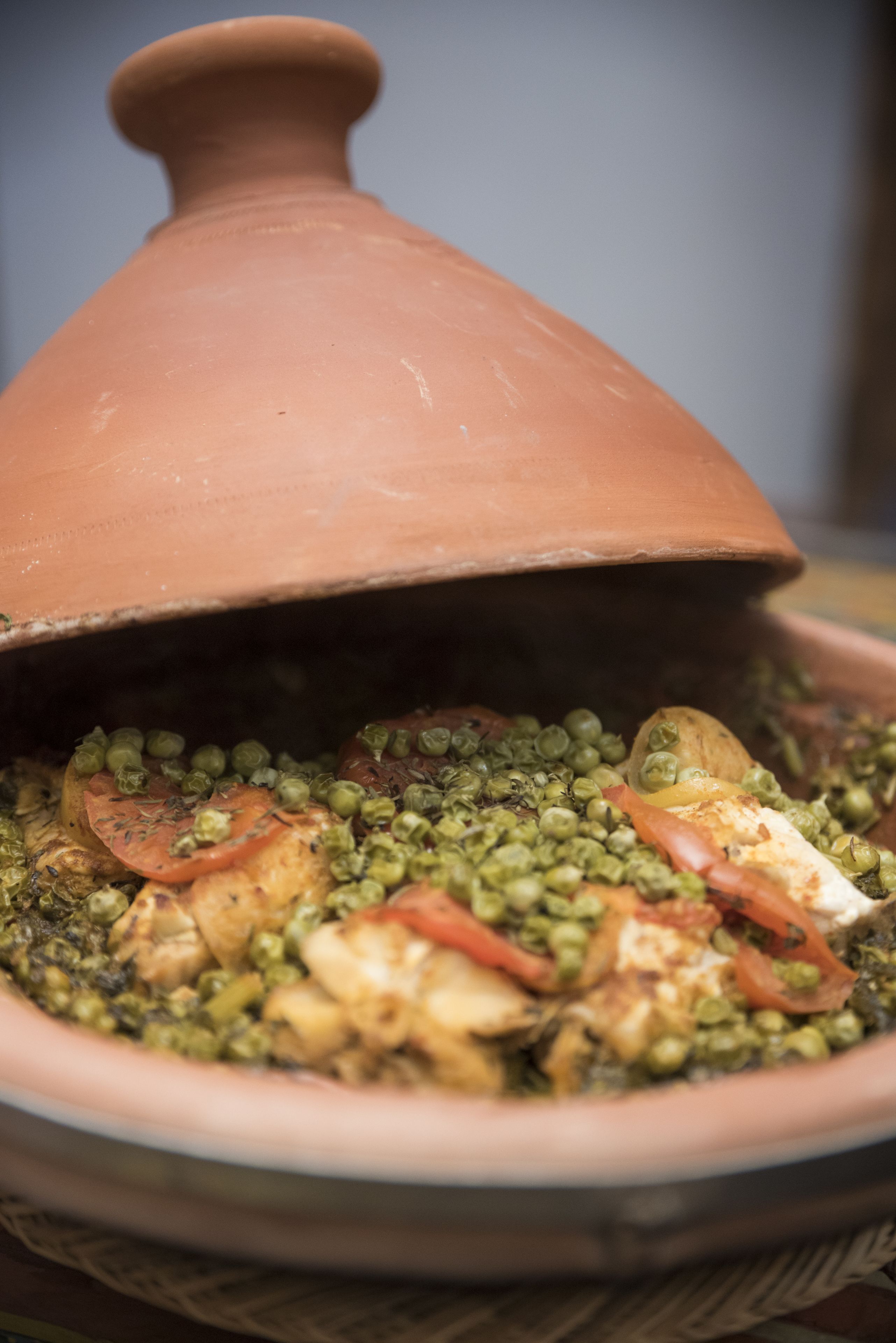 A traditional clay pot with a lid, filled with a stew containing peas, tomatoes, and other vegetables.