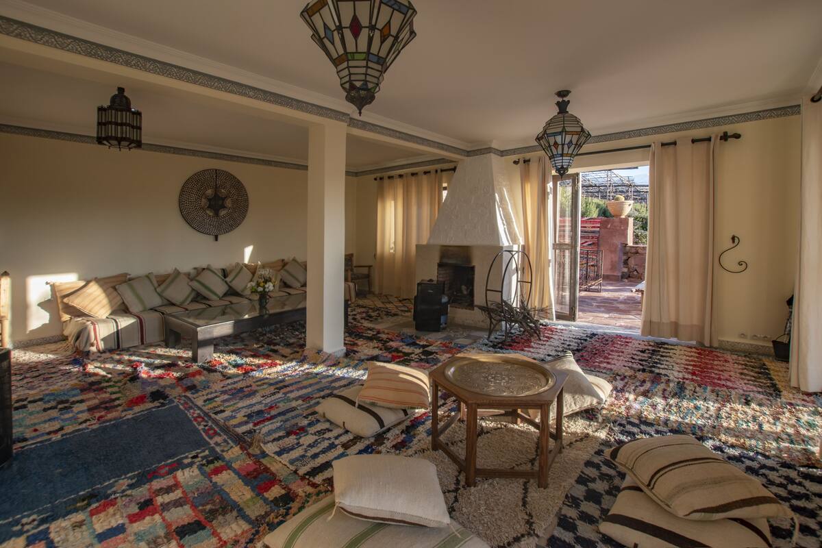 A spacious living room with a large, colorful rug, a sofa with cushions, a coffee table, and a fireplace.