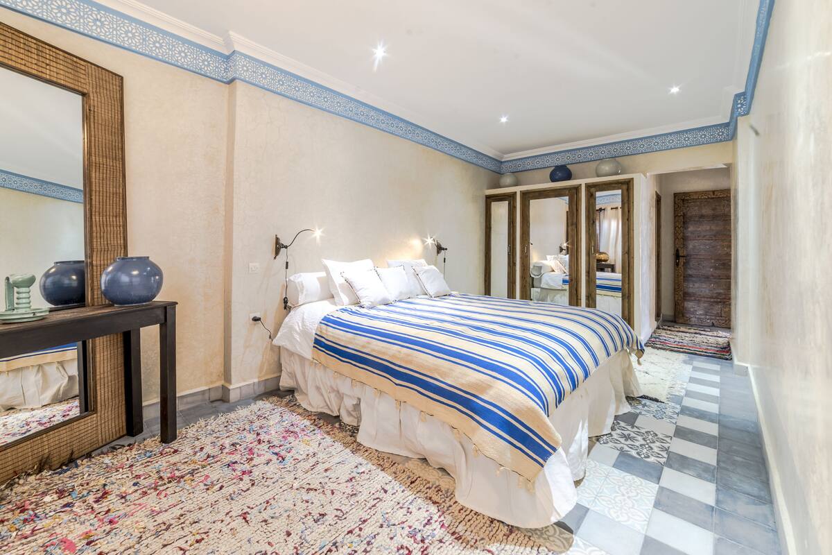 A bedroom with a large bed, a bedside table, a mirror, and a patterned rug.