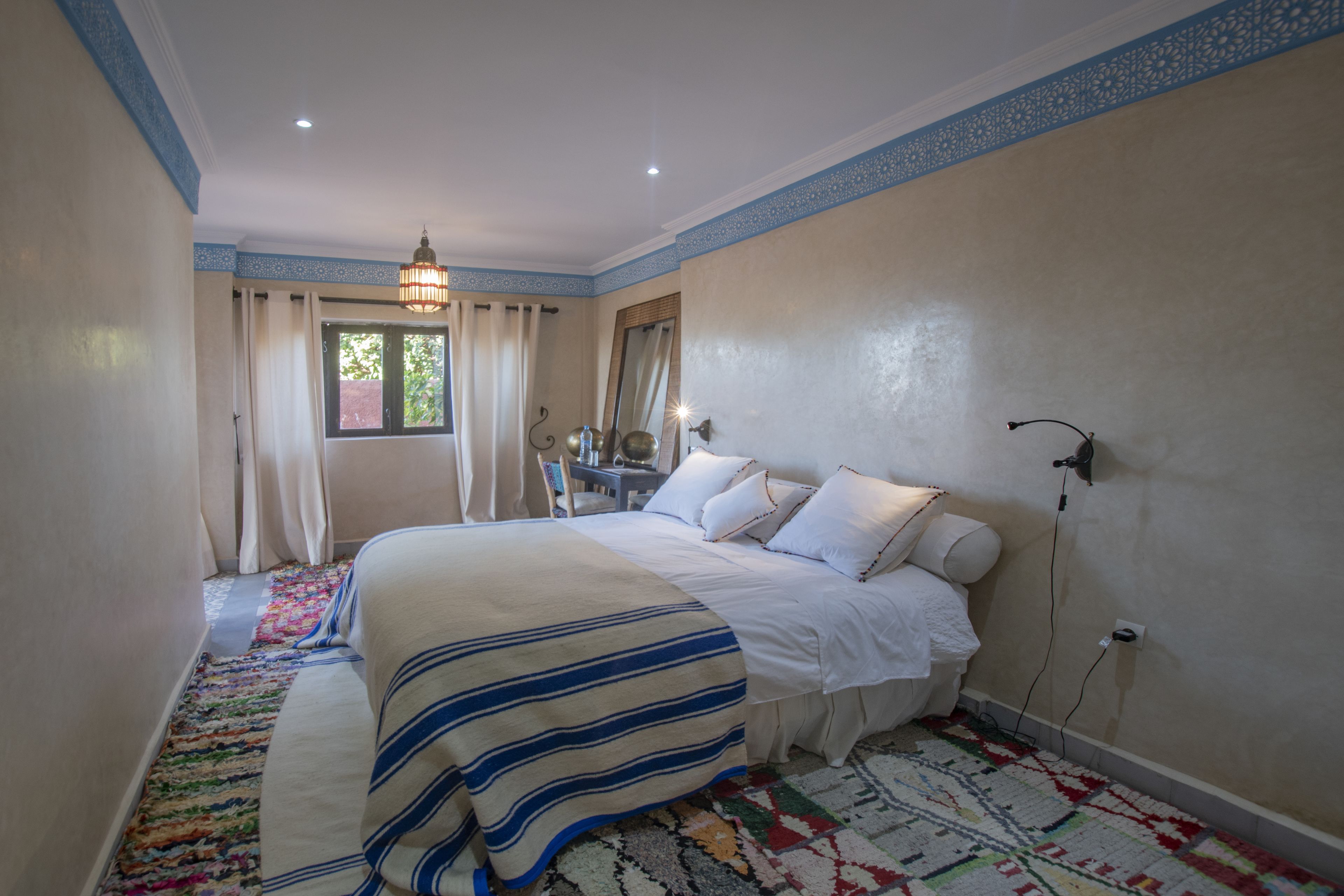Un dormitorio con cama, mesita de noche, espejo y ventana con cortinas.