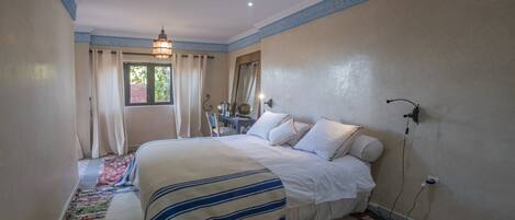 Un dormitorio con cama, mesita de noche, espejo y ventana con cortinas.
