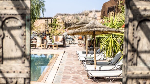 A pool area with lounge chairs and umbrellas, surrounded by stone walls and vegetation. - Dar Tafantant (Ourika)