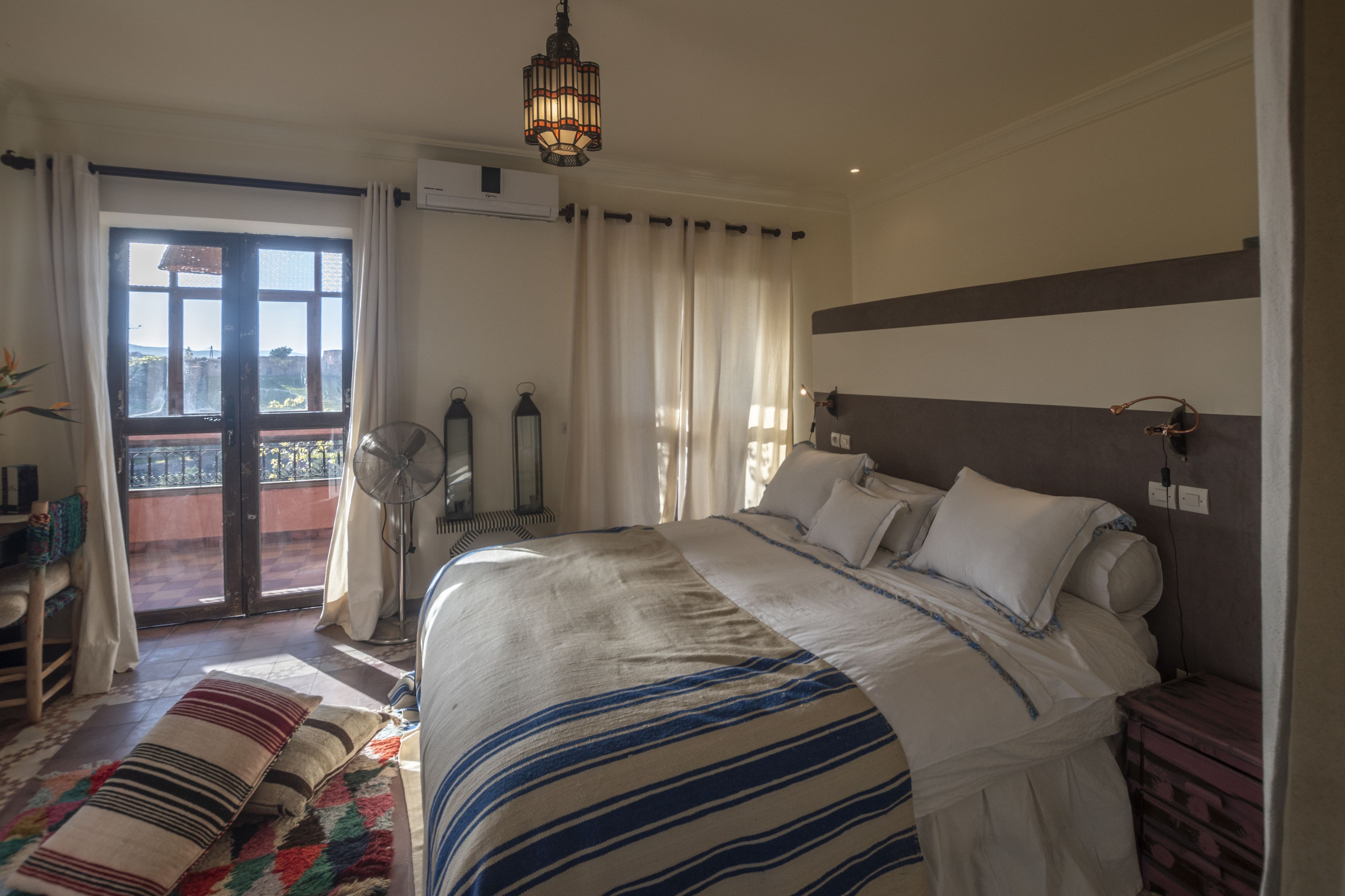 Een slaapkamer met een groot bed, een balkon met uitzicht, een plafondventilator en een hanglamp.