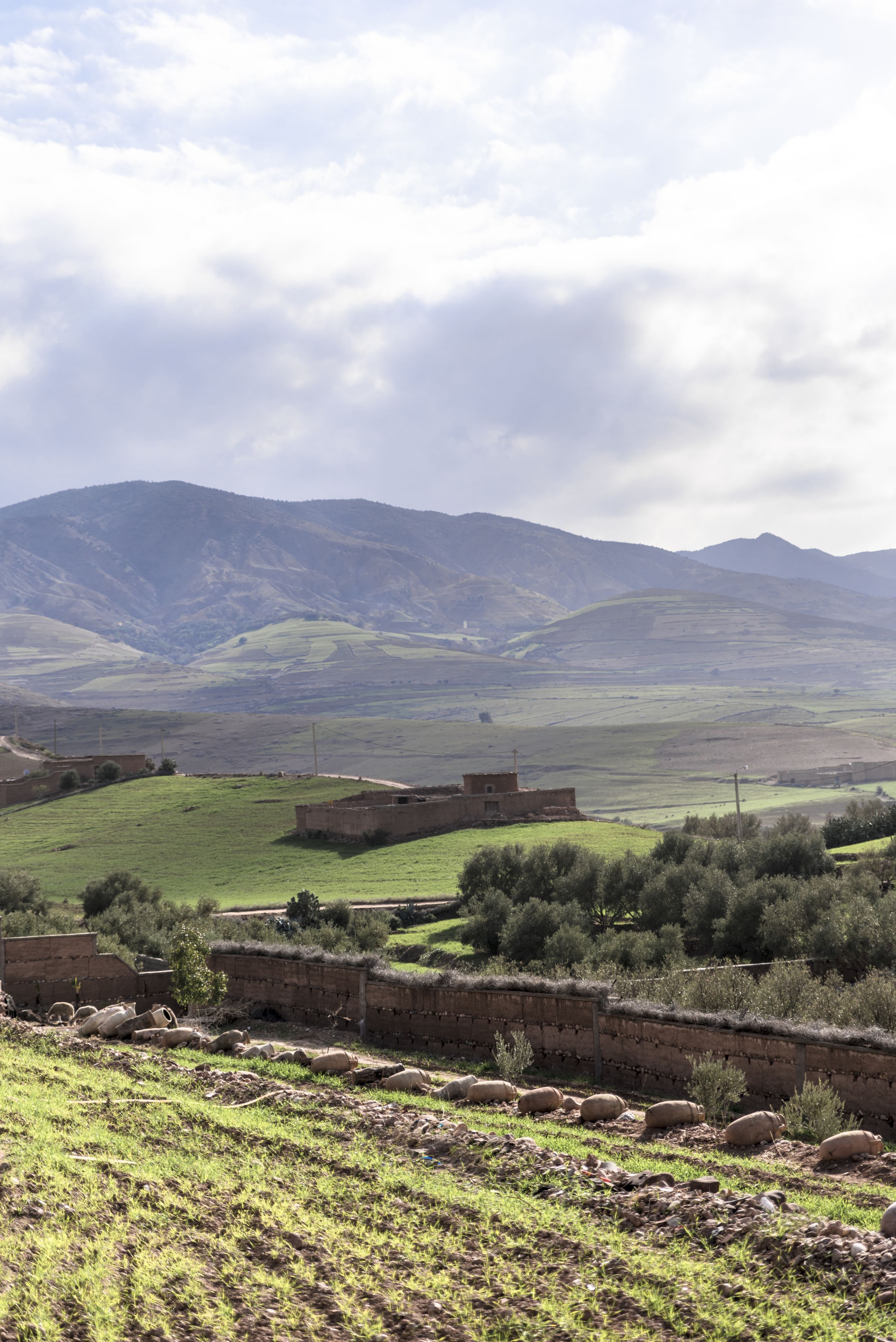 Paisaje rural con colinas onduladas, un muro de piedra y una cadena montañosa distante.
