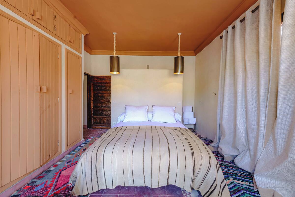 A bedroom with a large bed, wooden wardrobe, and a patterned rug.