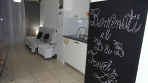 Ett litet, modernt rum med en säng, ett skrivbord och ett litet kök. Det finns en svart tavla där det står "Välkomna till B&B Travel Living".