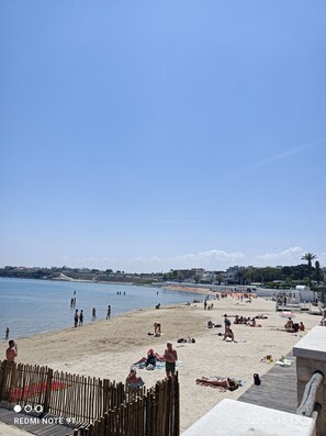 A beach with people sunbathing and swimming, a wooden fence, and a clear sky. - Travel And Living (Trani)
