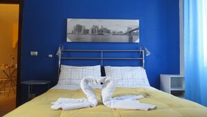 Ett hotellrum med en säng, en målning som föreställer en stadsbild och en blå vägg.