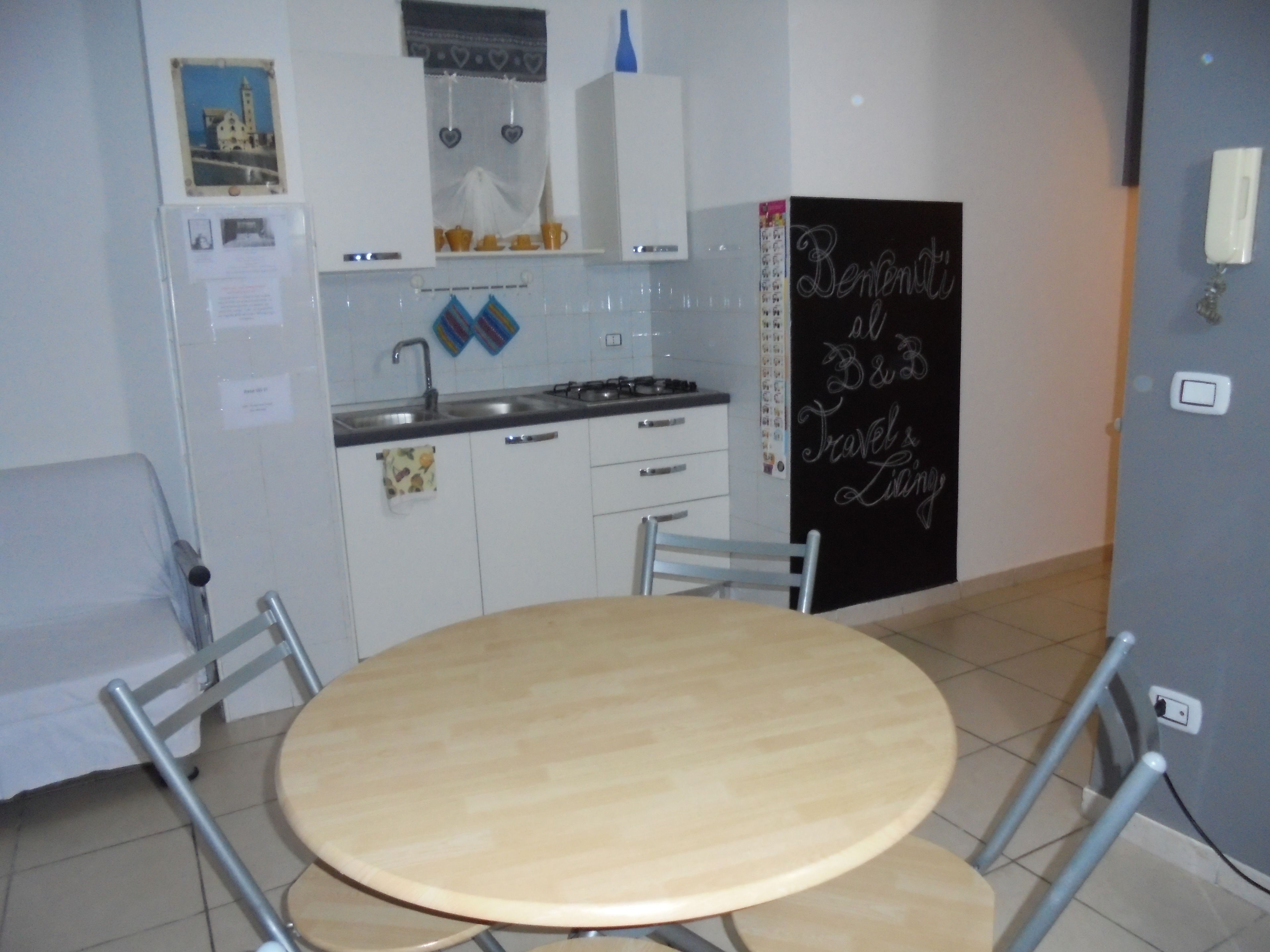 Una cocina compacta con armarios blancos, una estufa a gas y una pizarra con la inscripción 'Benvenuti al B&B'.