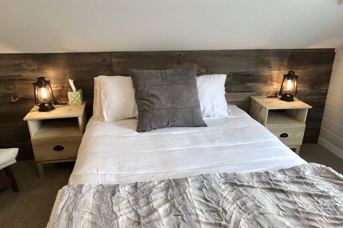 A bedroom with a large bed, two bedside tables with lanterns, and a wooden headboard.