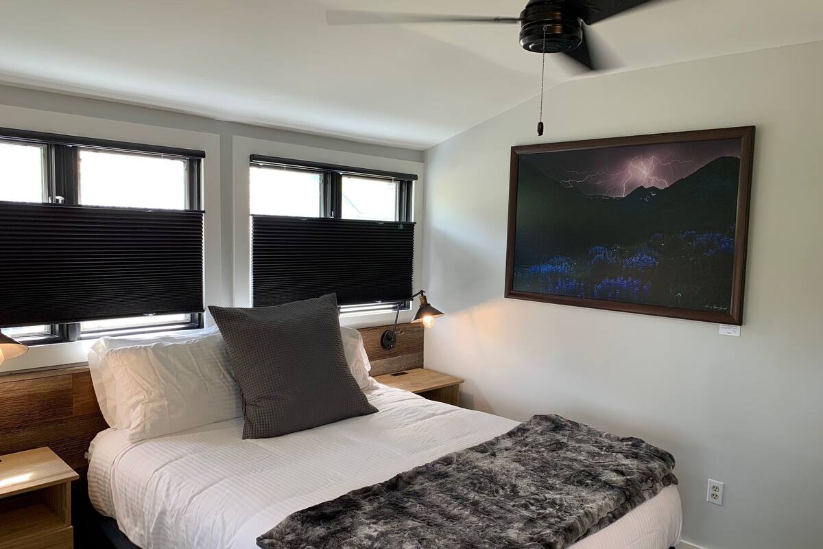 A bedroom with a bed, a ceiling fan, a nightstand, a lamp, and a framed picture on the wall.