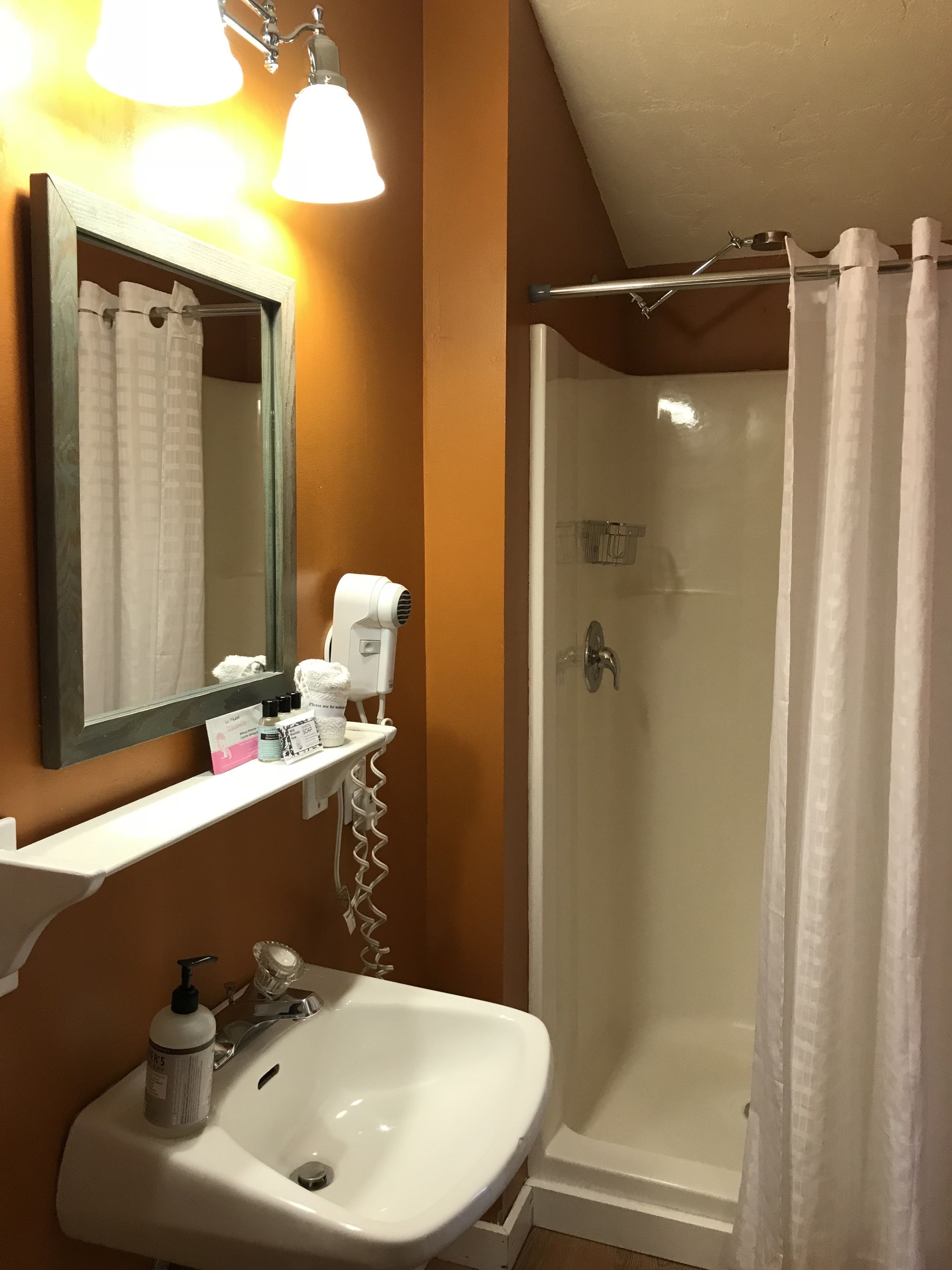 Une salle de bain avec un lavabo blanc, un miroir, une douche avec une porte en verre et une étagère contenant des articles de toilette.