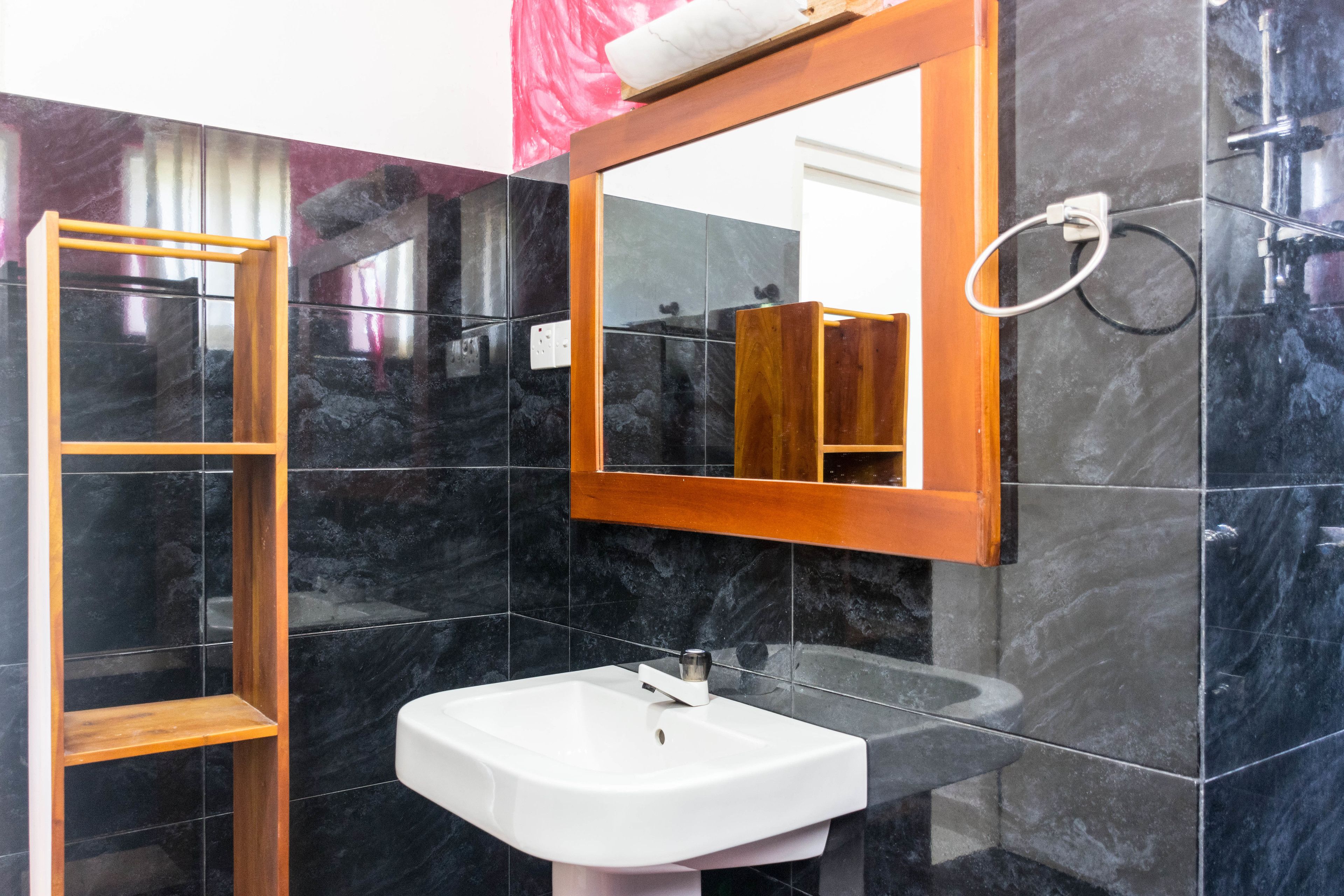Une salle de bain avec un lavabo blanc, une étagère en bois et un miroir auquel est accrochée une serviette au mur.