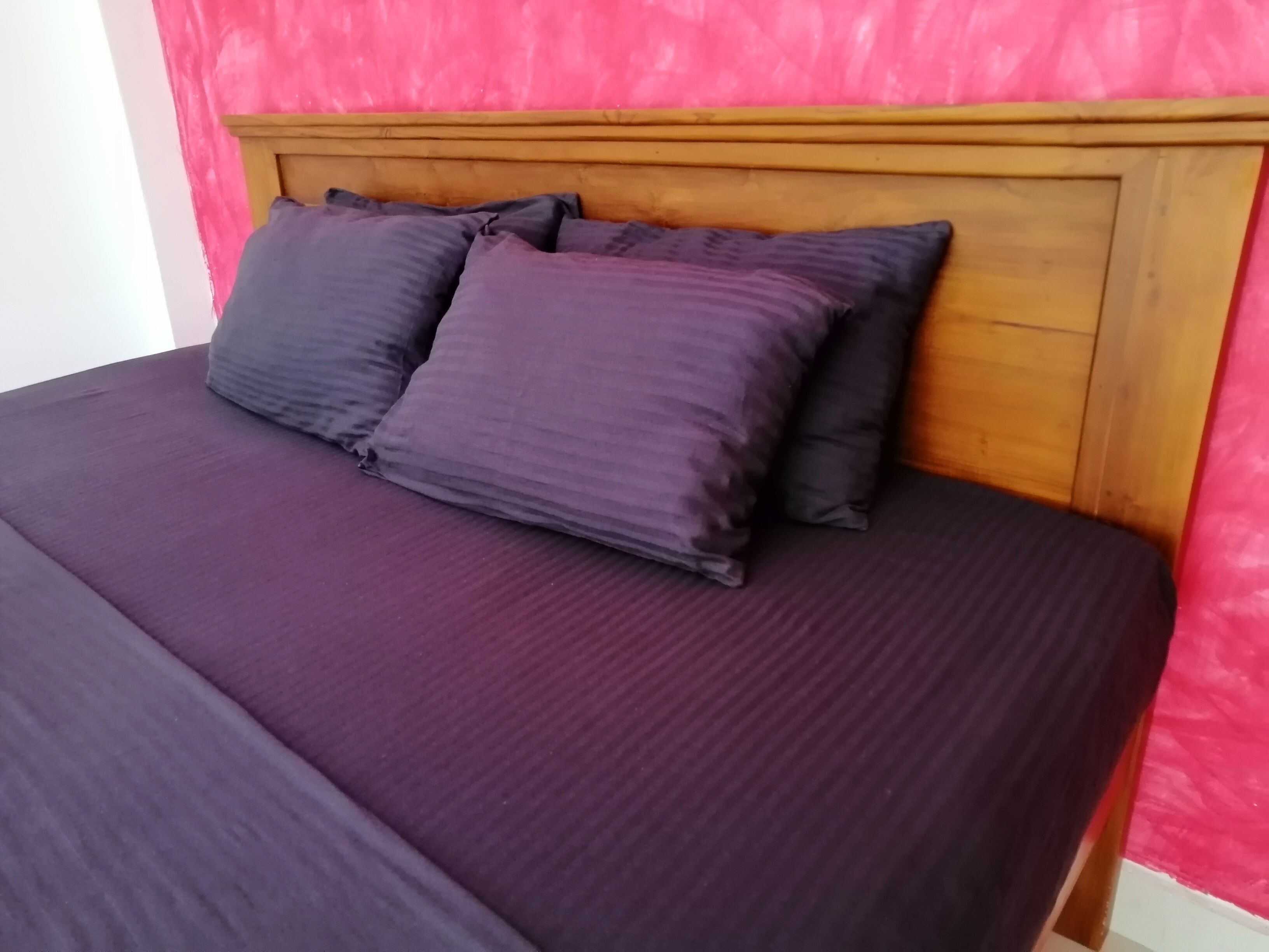 Un lit avec une tête de lit en bois et une literie de couleur violet foncé.