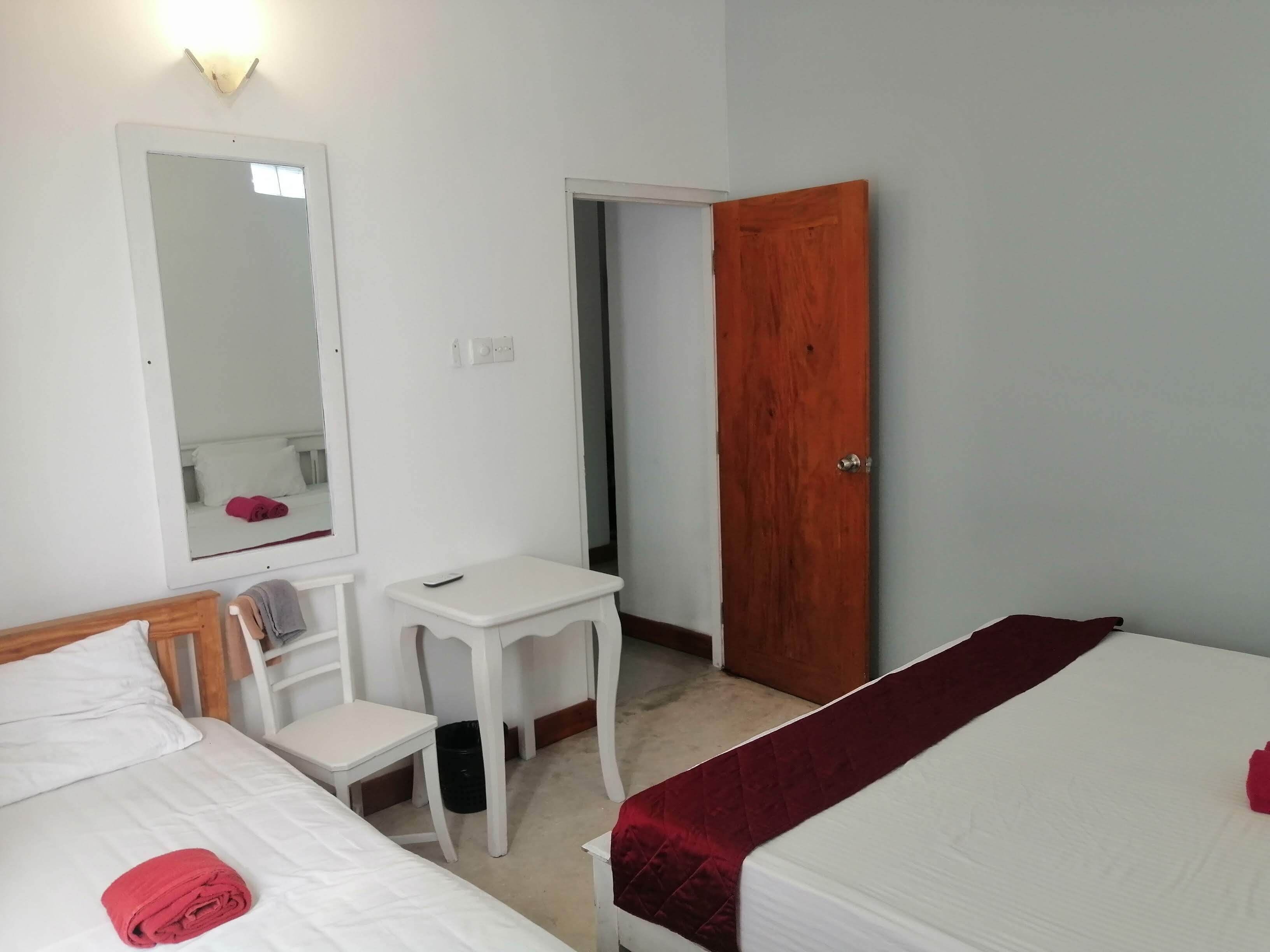 A hotel room with two beds, a desk, a chair, a mirror, and a door.