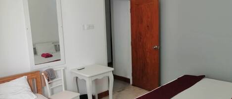 A hotel room with two beds, a desk, a chair, a mirror, and a door.