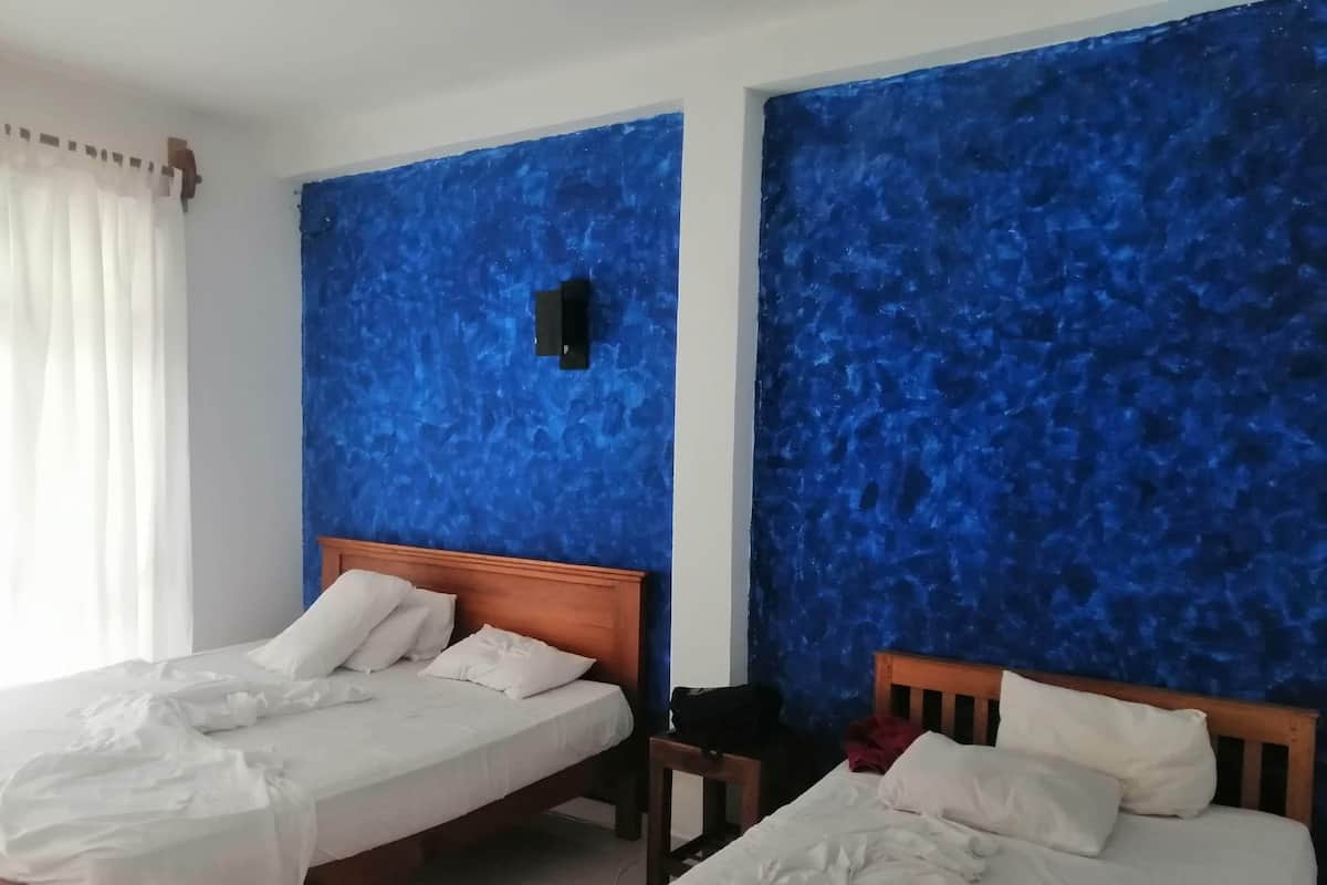A hotel room with two beds, a wooden headboard, and a blue textured wall.