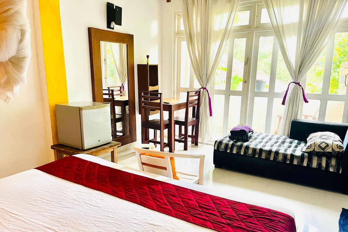 A hotel room with a large bed, a desk with a television, a chair, and a sofa.