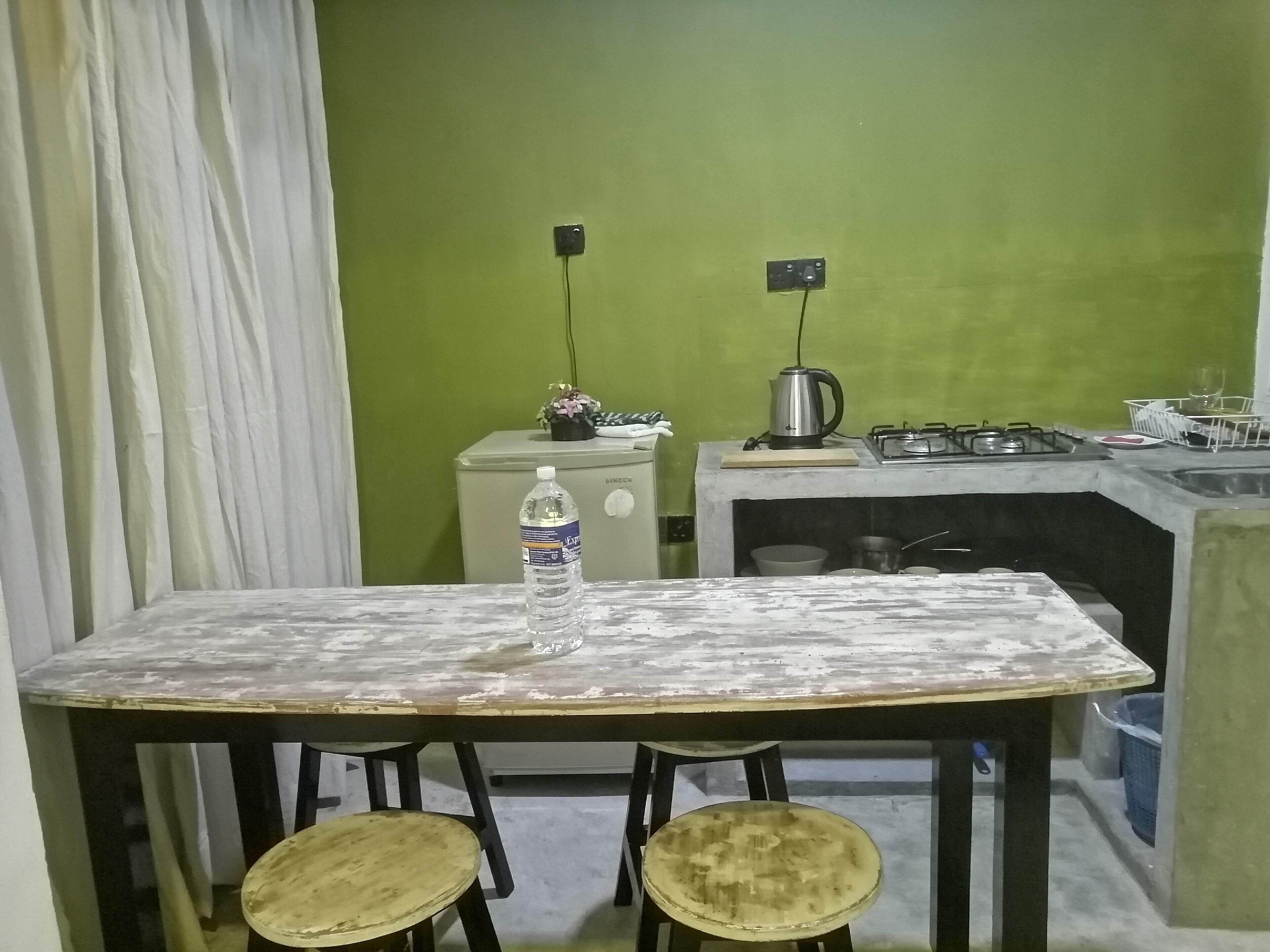 Una pequeña cocina con una mesa y dos taburetes, una botella de agua sobre la mesa y un hervidor en la encimera.