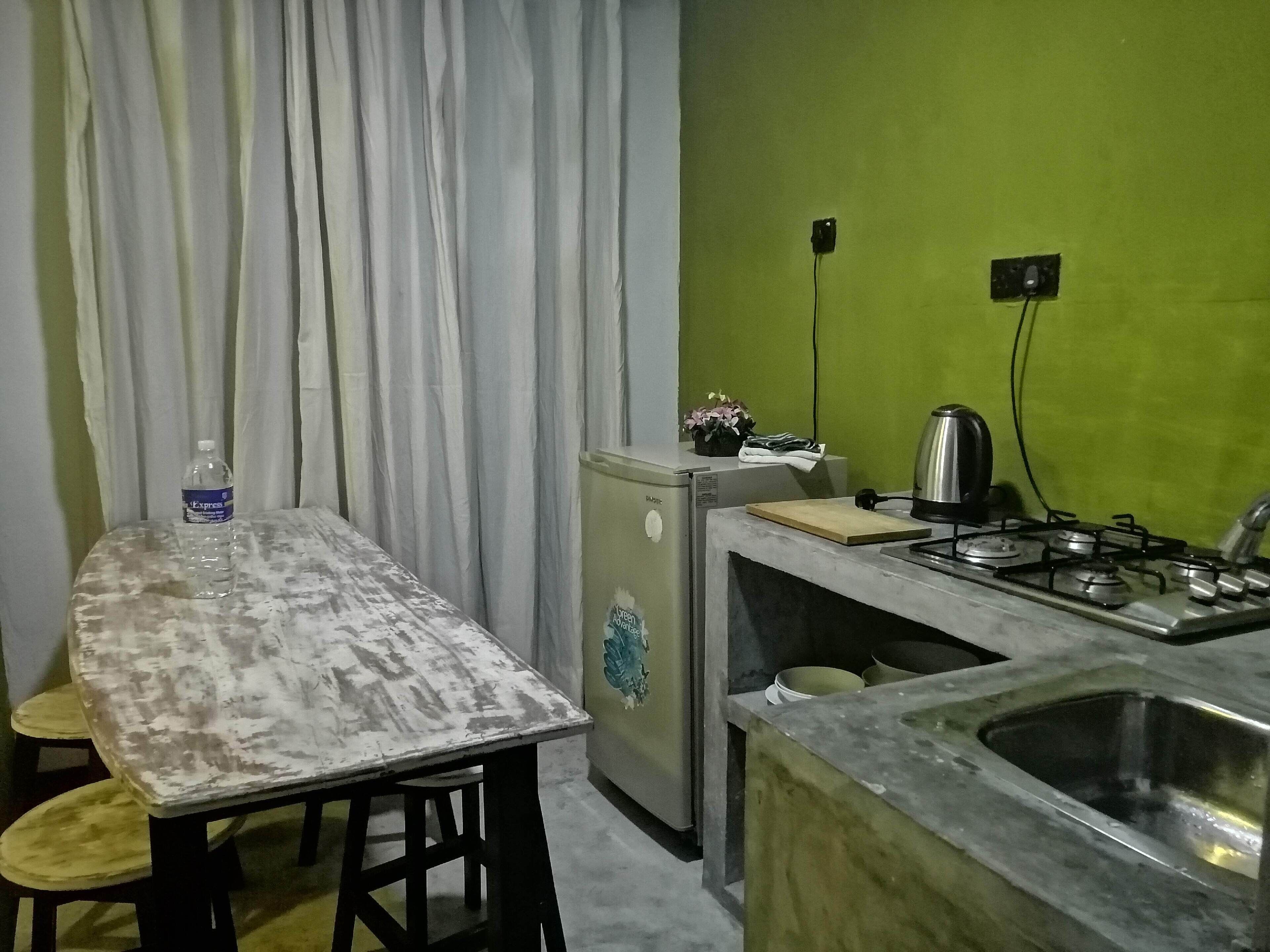 A compact kitchen with a dining table, chairs, a refrigerator, a gas stove, and a sink.