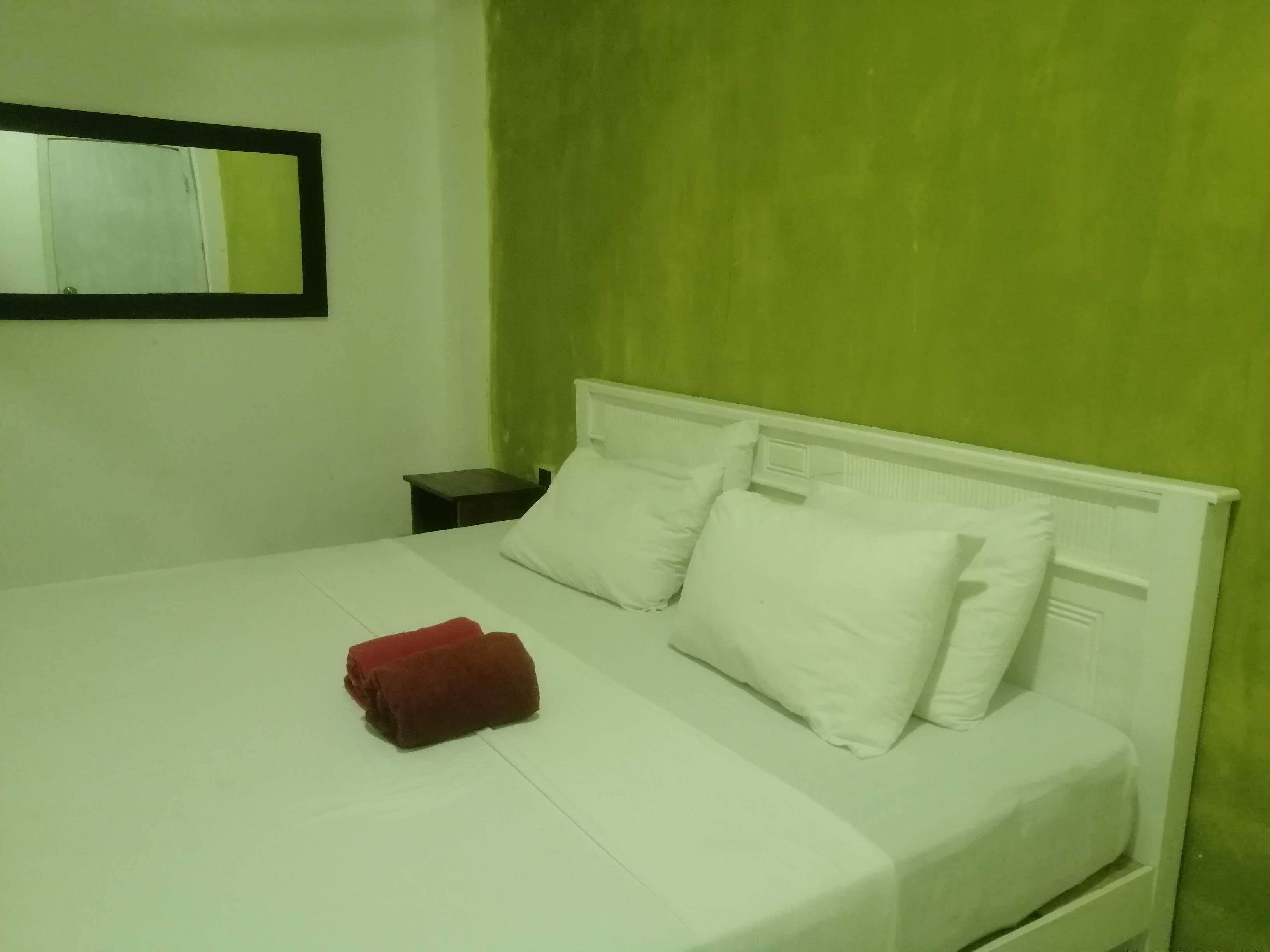 Una cama con ropa de cama y almohadas blancas, una toalla roja, una mesita de noche y un espejo en la pared.
